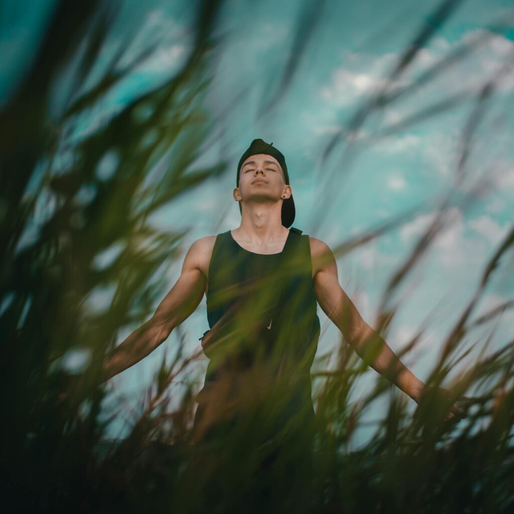 About Mindmotion A young man relaxes and meditates among tall grass outdoors, eyes closed, embracing nature.