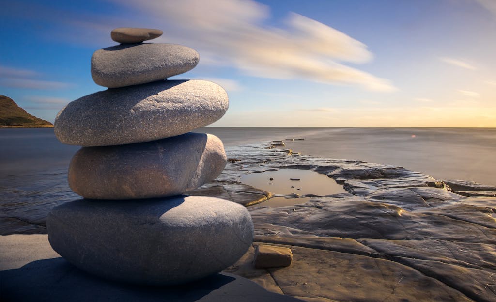 Home About - Mindmotion. A serene stack of stones on the rocky seashore during a peaceful sunrise, embodying balance and zen.
