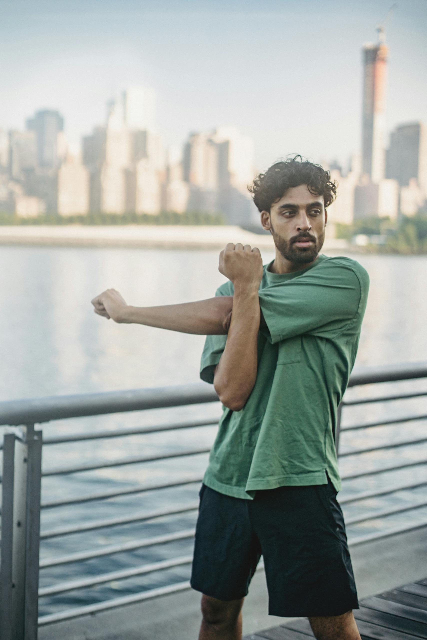 Routines and Habits A man in a green shirt stretches by the waterfront with a city skyline in the background.