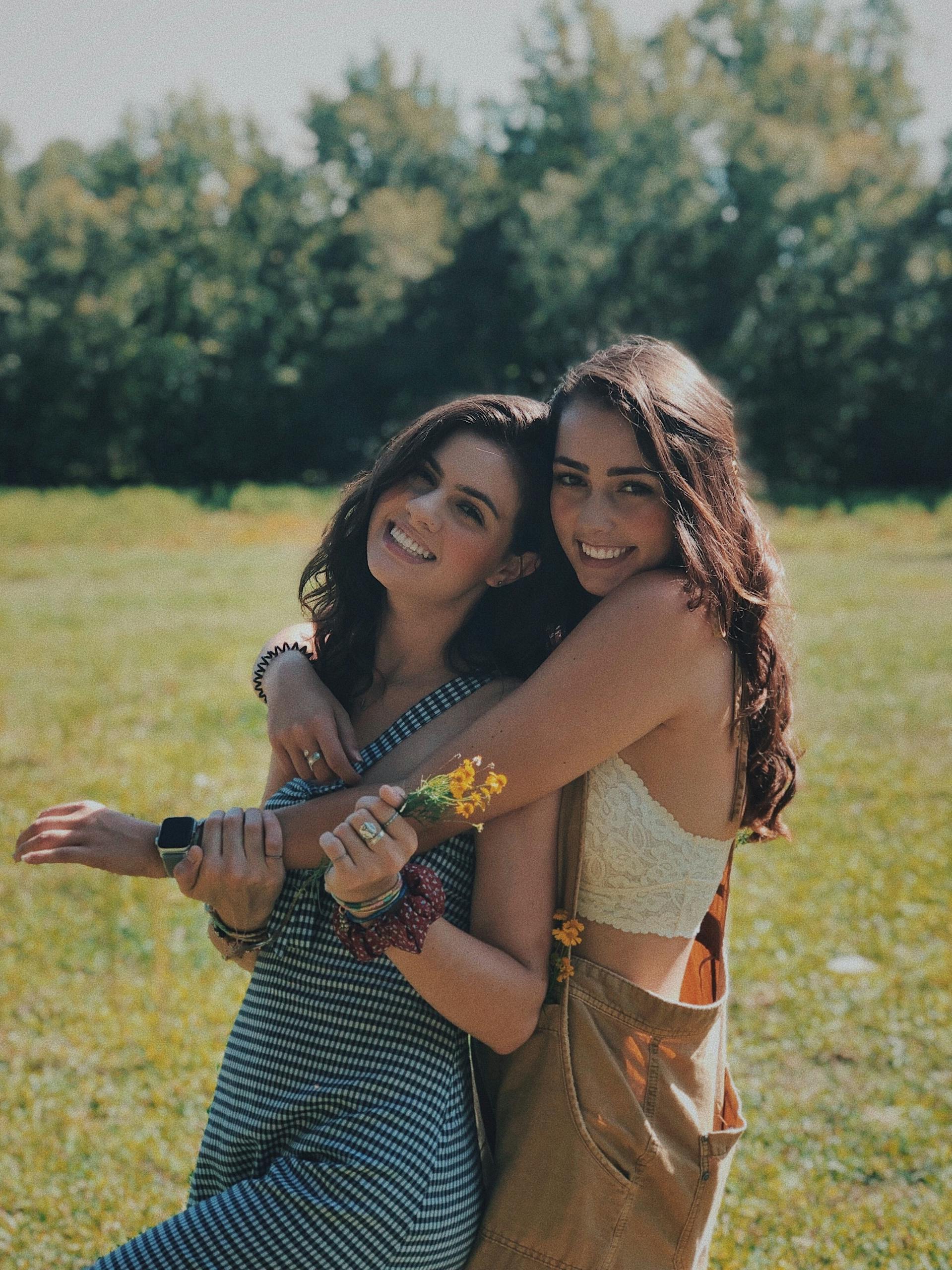 Friendships Two smiling sisters embracing in a sunlit park, enjoying a warm summer day together.