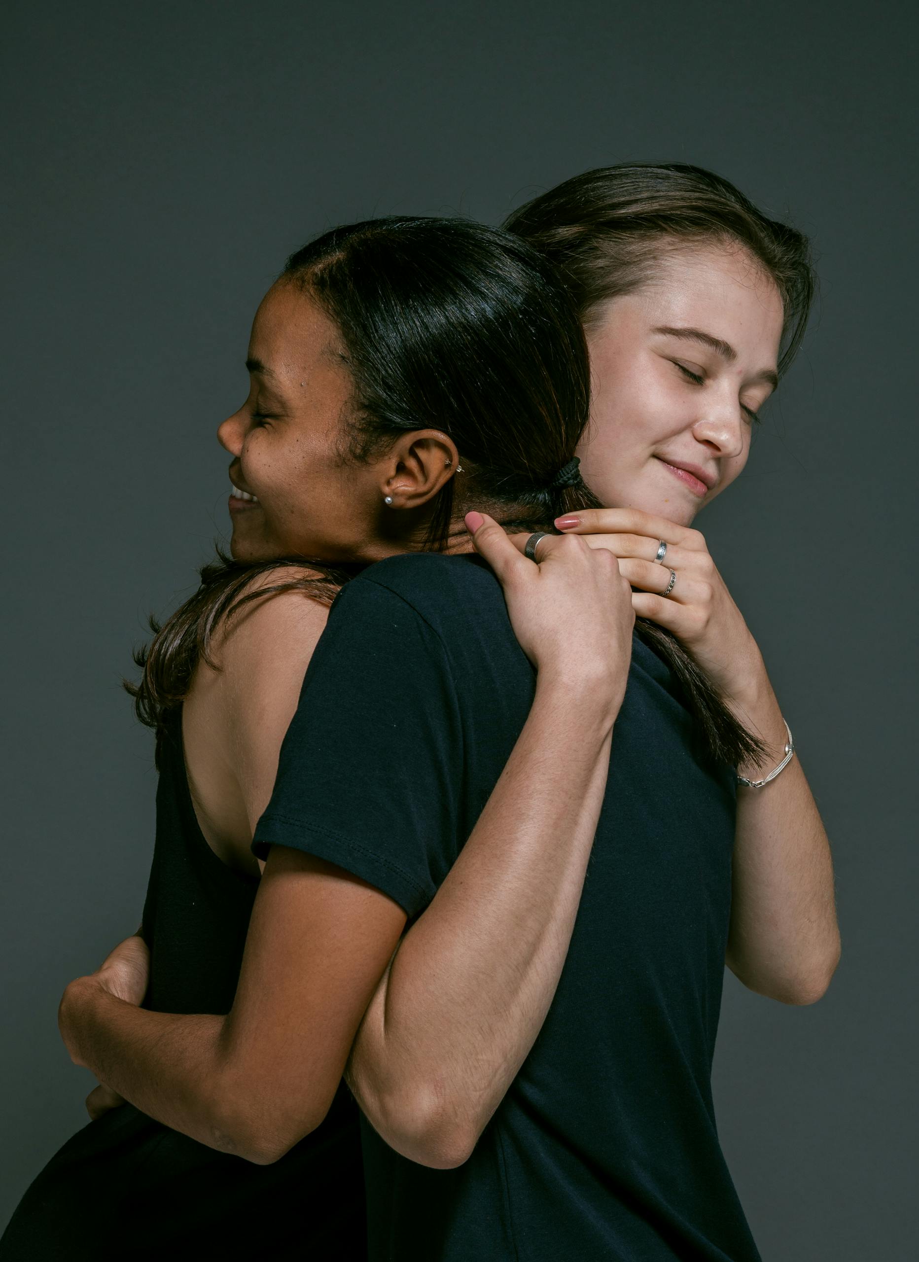 Forgiveness Two women of different ethnicities share a warm hug, symbolizing love and friendship against a gray backdrop.